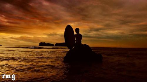 Silhouette father with daughter sitting on beach against sky during sunset