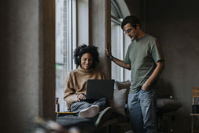 Smiling businesswoman using laptop by male colleague standing in creative office