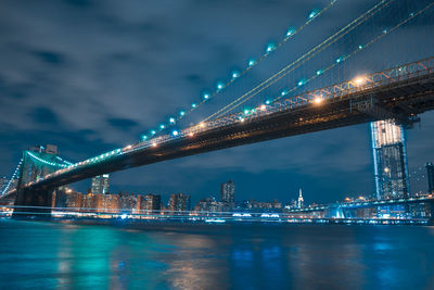 Illuminated bridge over river against sky at night