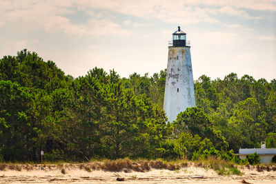 Lighthouse amidst trees and buildings against sky