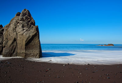 Rock formation on beach against clear blue sky