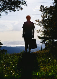 Rear view of man walking on landscape against sky