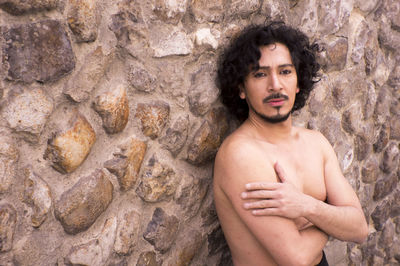 Portrait of shirtless mature man standing against wall