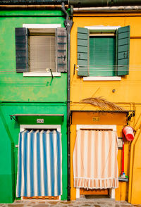 Exterior facade of houses colored green and yellow with typical striped curtains in burano