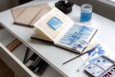 An open watercolor sketchbook lies on a white table.