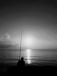 Silhouette man fishing in sea against sky