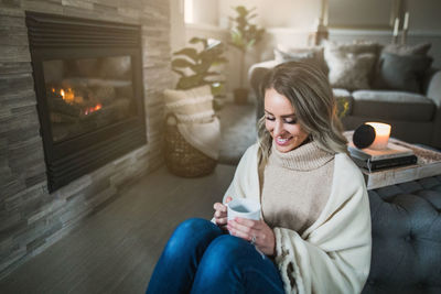 Smiling young woman holding coffee while sitting at home