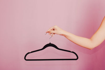 Woman holding black hanger. studio photo with light pink background.