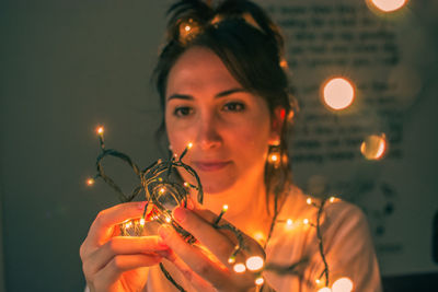 Portrait of young woman holding illuminated lighting equipment