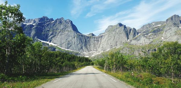 Road amidst trees and mountains against sky