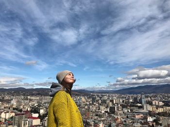 Woman looking away while standing against cityscape and sky