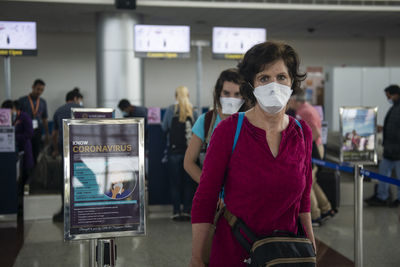 Middle aged woman wearing a face mask walking by a coronavirus warning at an airport.