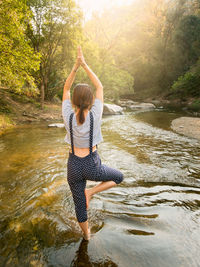 Rear view of young woman practicing tree pose in stream