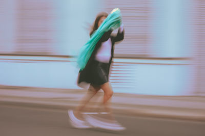 Side view of woman holding scarf running on road in city