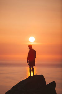 Silhouette man standing on rock against sky during sunset