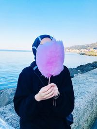 Woman covering face with purple cotton candy against sea