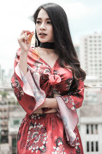 Smiling young woman standing against sky in city