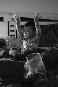 Cute baby boy with arms raised sitting on bed at home