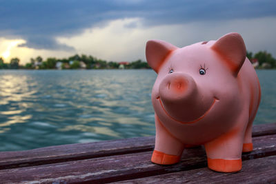 Close-up of piggy bank on table at lake against sky