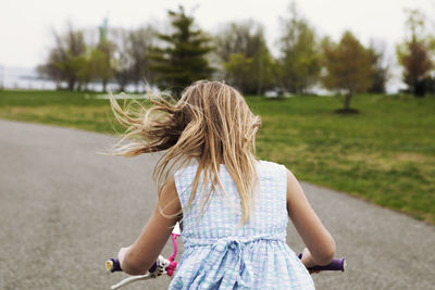 Side view of girl riding bicycle on road by field