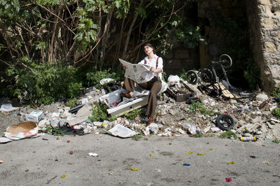 Man sitting on garbage bin against trees