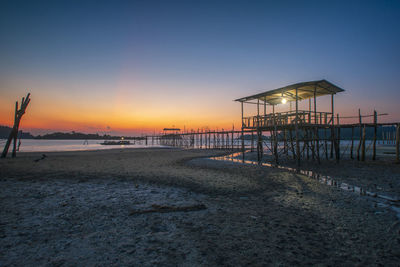 Pier on beach against sky during sunset