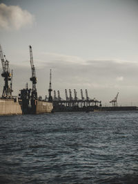 Cranes at commercial dock against sky