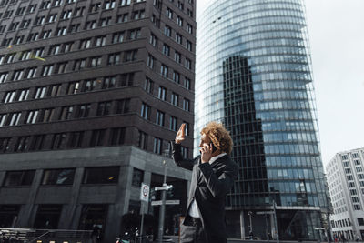 Businessman shielding face and talking on mobile phone in city