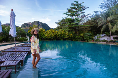 Woman standing by swimming pool against trees