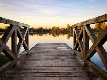 Wooden jetty leading to pier over lake against sky