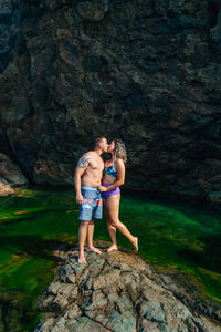 Young couple kissing while standing on rock by sea