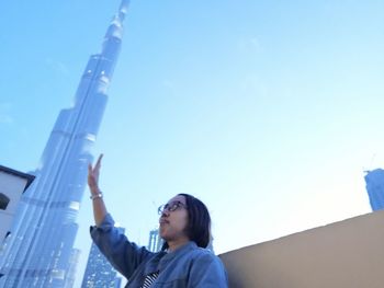 Low angle portrait of young woman looking at camera against blue sky