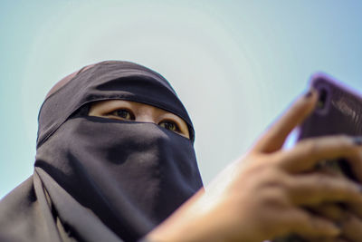 Portrait of female with black hijab veil close face show her eyes only blue sky background 