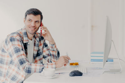 Smiling man talking on phone while using computer