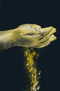 Cropped hands of person holding powder paint against black background