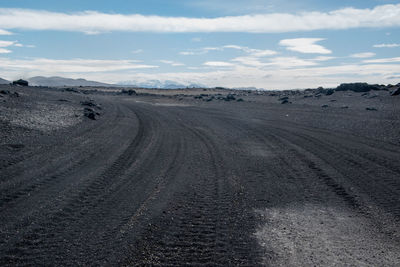 Dirt road passing through landscape against sky