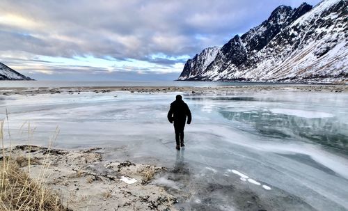 Rear view of man walking on frozen lake against snowcapped mountain
