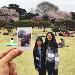 Cropped image of hand holding polaroid against mother and daughter at park