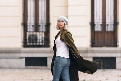 Portrait of young woman standing against wall in city