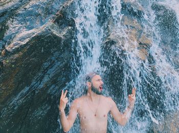 Man gesturing peace sign enjoying in waterfall against rock formation