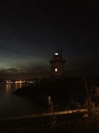 Illuminated building by sea against sky at night