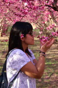 Beautiful woman smelling the pretty pink flowers of peach tree.