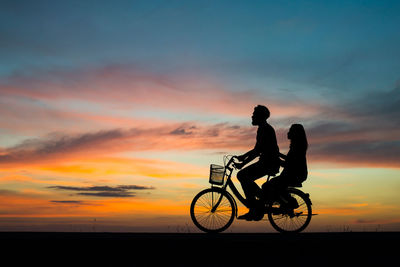 Silhouette man and woman on bicycle against sky during sunset