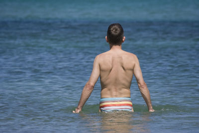 Rear view of shirtless man at sea