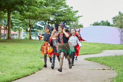 Girls in halloween costumes running on footpath at park