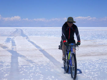 Portrait of mid adult man riding bicycle at salar de uyuni against blue sky