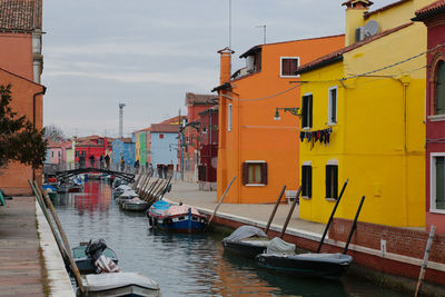 Boats moored on canal by buildings against sky in city