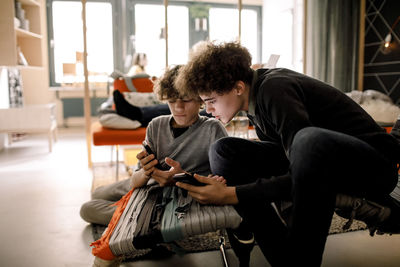 Brothers sharing mobile phone in living room with sister and father in background