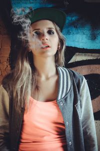 Close-up portrait of young woman smoking while standing against wall