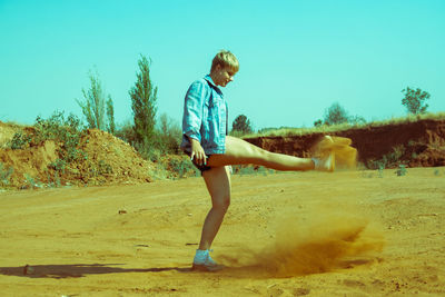 Full length of woman kicking sand against clear sky